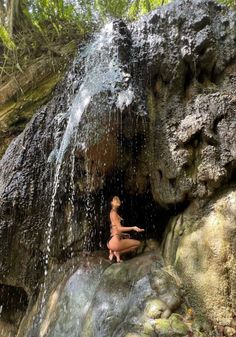 a naked woman sitting on top of a rock next to a waterfall in the woods