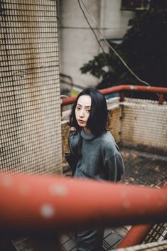 a woman standing in front of a gate with her hand on her shoulder and looking at the camera