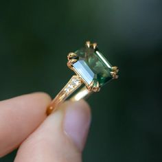 a close up of a person's hand holding a ring with an emerald colored stone