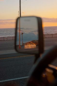 the reflection of a house in a rear view mirror on a road next to the ocean