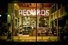 a store front with neon lights and records on the wall in it's windows