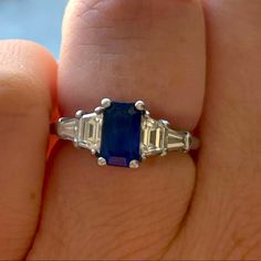 a woman's hand holding an engagement ring with two emeralds and three baguettes