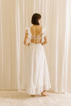 the back of a woman wearing a white dress with ruffles on her shoulders