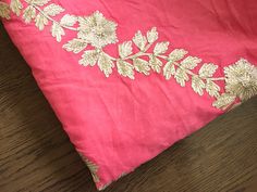 a pink and gold dress laying on top of a wooden floor next to a pillow