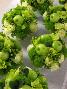 an arrangement of green apples and flowers on a counter