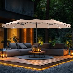 an outdoor living area lit up at night with candles on the table and umbrella over it