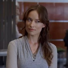 a woman with long brown hair wearing a gray shirt and silver necklace standing in an office