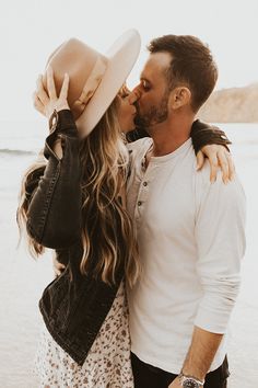 a man and woman kissing on the beach with their arms around each other while wearing hats