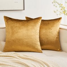 two gold pillows sitting on top of a couch next to a vase with white flowers