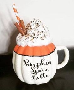 a pumpkin spice latte mug with whipped cream and cinnamon sticks in it, sitting on a table