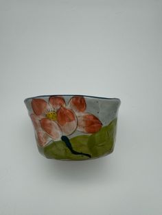 a small bowl with flowers painted on the side and green leaves in the middle, sitting on a white surface