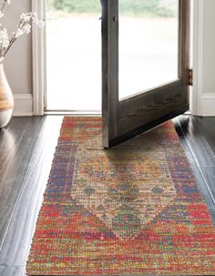 an old rug is sitting on the floor in front of a door and vase with flowers