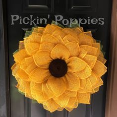 a yellow sunflower wreath hanging on the front door of a house with words pickin'poppies written on it