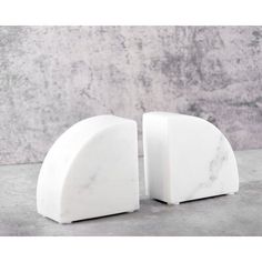 two white marble bookends sitting on top of a cement floor next to a wall