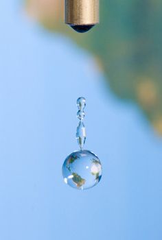 a drop of water hanging from a faucet with a blue sky in the background