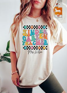 🍎✏️ Celebrate the start of the school year with our Comfort Colors® Personalized Kindergarten Teacher Shirt! This retro-inspired tee is perfect for kindergarten teachers heading back to school. Show your appreciation with a custom gift that combines style and sentiment. #KindergartenTeacherShirt #BackToSchool #ComfortColorsShirt Comfort Colors® Personalized Kindergarten Retro Teacher Shirt fits like a well-loved favorite. Super soft cotton and excellent quality print make one to fall in love with it over and over again. Custom Name Back to School Pre School Teacher Tee, Gift For Kindergarten Teacher. These are Unisex Garment-Dyed T-shirt made 100% with ring-spun cotton. Shirts look retro and vintage. The soft-washed, garment-dyed fabric brings extra coziness to your wardrobe while the rel Multicolor Letter Print T-shirt For School Events, Educational College T-shirt With Letter Print, Casual Text Print T-shirt For Daycare, White Graphic Print T-shirt For Teaching, Fun Letter Print T-shirt For School Events, White T-shirt With Letter Print For Daycare, Crew Neck T-shirt With Name Print For Daycare, Teacher Appreciation School Spirit T-shirt, Cotton T-shirt With Name Print For Daycare