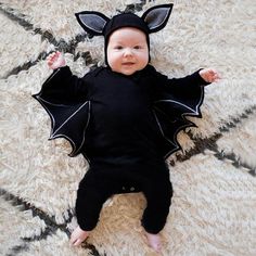 a baby wearing a bat costume laying on top of a rug with his hands in the air