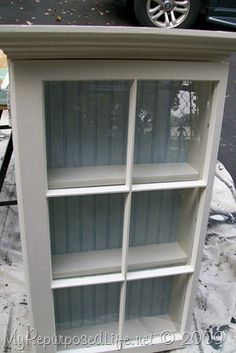 a white bookcase sitting on top of a snow covered ground next to a black car