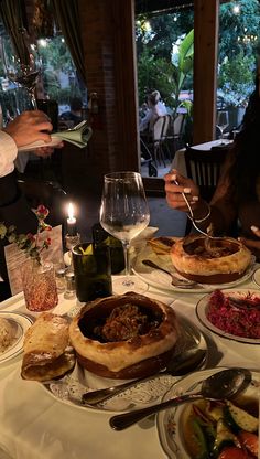 two people sitting at a table with food and wine in front of them on plates