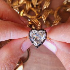 a heart shaped diamond being held by someone's hand in front of a gold chain