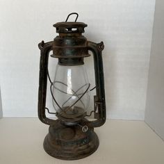 an old fashioned lantern is sitting on a table in front of a white wall,