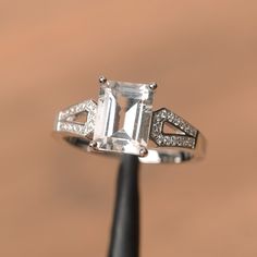 an emerald cut diamond ring sitting on top of a black piece of metal with diamonds around it