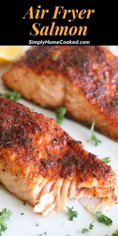 two salmon fillets on a white plate with parsley and lemon wedges in the background