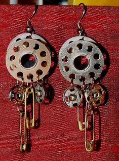 two silver and gold earrings with chains hanging from it's sides on a red cloth