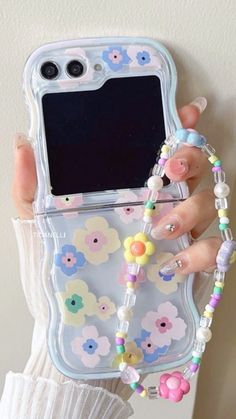 a woman is holding up her phone case with beads and flowers on the front cover