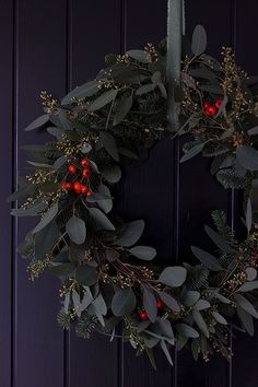 a wreath with berries and greenery hanging on a door handle, in front of a purple painted wall