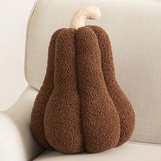 a brown stuffed animal sitting on top of a white couch next to a pillow that is shaped like a pumpkin