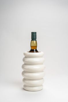 a bottle of whisky sitting on top of a white vase with a green cap in it