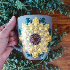 a hand holding a coffee cup with yellow and green designs on the outside, surrounded by greenery