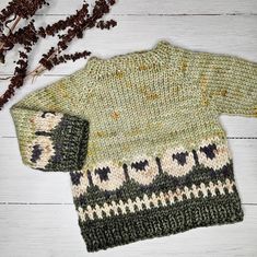 a green sweater and hat sitting on top of a white wooden floor next to dried flowers