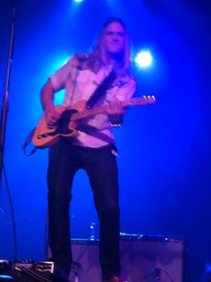 a man standing on top of a stage with a guitar in his hand and lights behind him