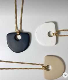 three necklaces with different shapes and colors hanging from gold chains on a white surface