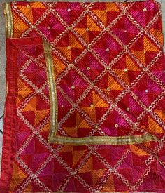 an orange and red cloth with gold trimmings on the edges, sitting on top of a tile floor