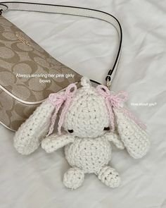 a crocheted stuffed animal sitting next to a purse on a white bed sheet