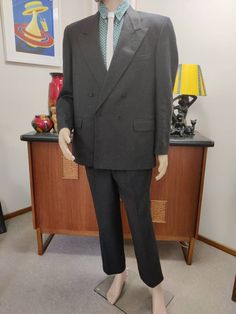 This is an 80s suit by the Pierre Cardin label in a charcoal grey medium weight wool fabric. The inside pocket says 107cm short. The jacket is very well cut and finished, is a box shape somewhat oversized in a loose fit, has wide sharp lapels, firm shoulder padding, a double breasted closure and plenty of internal pockets and is charcoal grey lined. The pants are a slim cut with side seam pockets and two small pleats at the front. There is a good seam allowance at the hem should you need it for Gray Double-breasted Suit For Business, Gray Double-breasted Business Suits, Gray Double-breasted Formal Suit, Classic Gray Double-breasted Suit, Gray Fitted Double-breasted Suits, Vintage Double-breasted Suits For Workwear, Vintage Double-breasted Suits For Tailoring, Retro Double-breasted Formal Blazer, Vintage Double Breasted Suit With Notch Lapel For Work