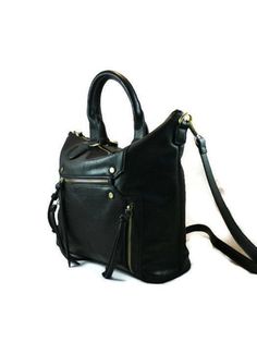 a black leather handbag with zippers on the front and shoulder strap, sitting against a white background