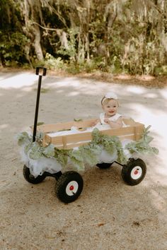 a baby is sitting in a wagon on the sand with green plants and leaves attached to it