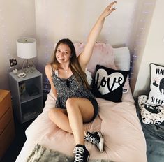 a woman sitting on top of a bed with her arms in the air and smiling