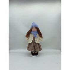 a doll with long brown hair wearing a blue hat and scarf is standing in front of a white background