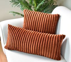 two orange pillows sitting on top of a white couch next to a potted plant