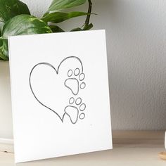 a white card with a heart and paw prints on it next to a potted plant