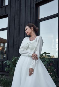 a woman in a white dress is standing near a black building and looking off into the distance