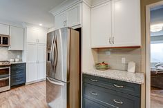 Kitchen remodel with white upper cabinets, a grey backsplash, light granite countertops, new vinyl plank flooring, and farm sink under the bay window Whale Gray Cabinets, Silestone Ocean Storm Countertop, Single Bowl Kitchen Sink Lowe's, Hampton Bay Brindle Cabinets