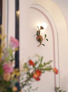 a wall mounted light with flowers in the background