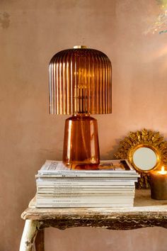 a lamp sitting on top of a wooden table next to a pile of books and a mirror