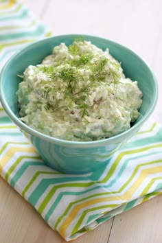 a blue bowl filled with cucumber salad on top of a striped napkin next to a fork